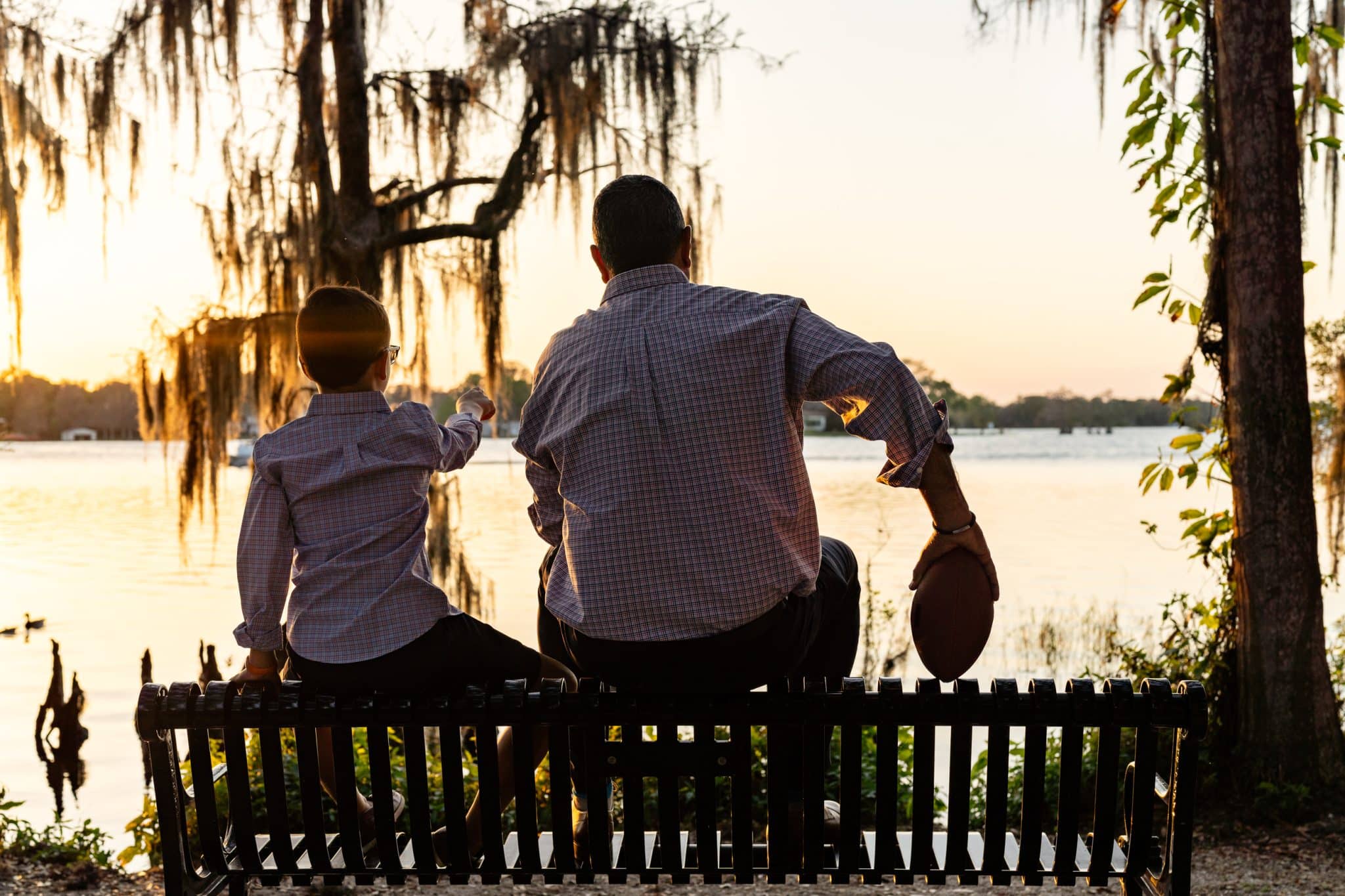 Jim and son sitting on park bench looking out at a Central Florida lake at sunset