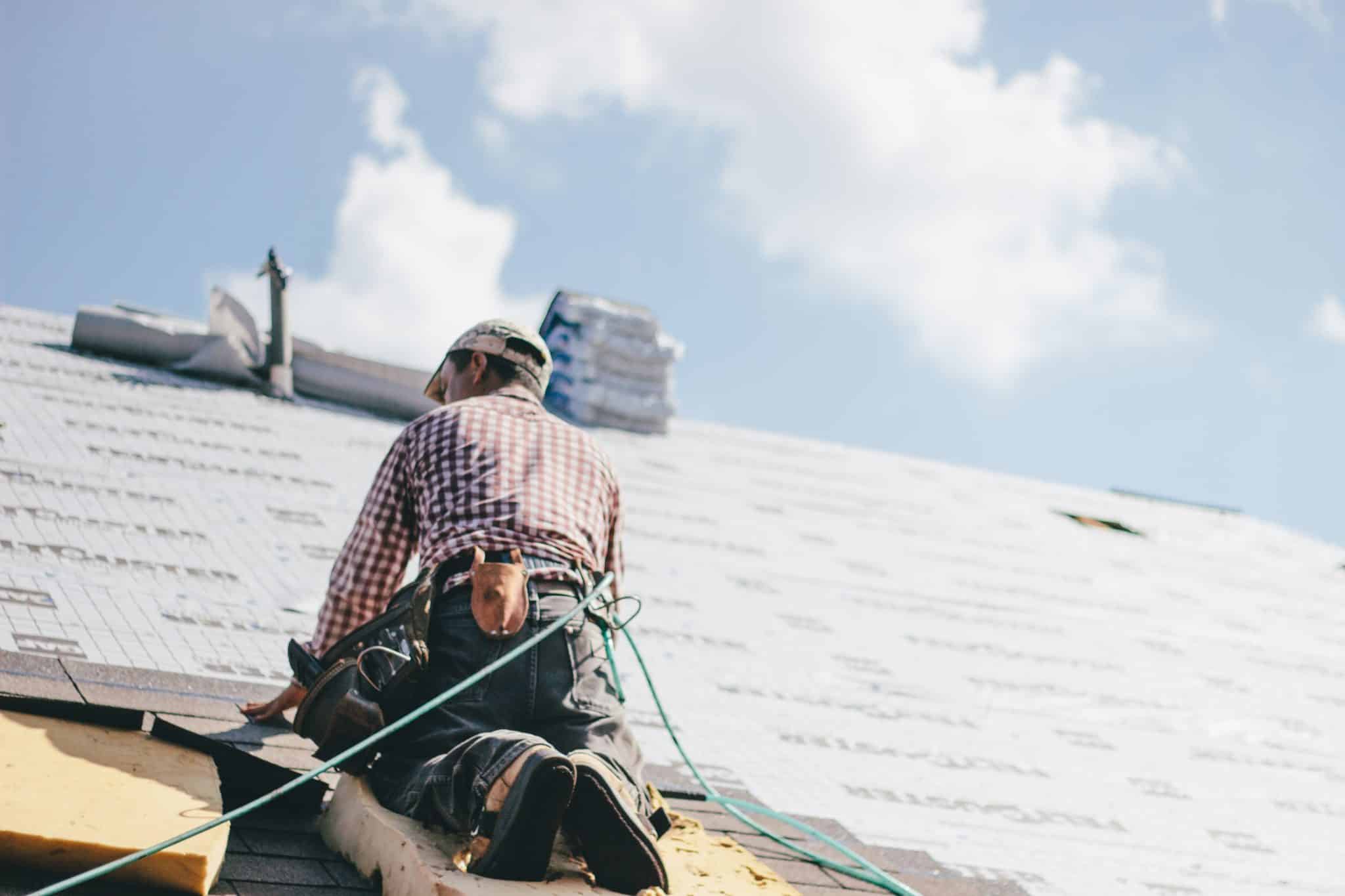 A roofer installing shingles on the roof of a house